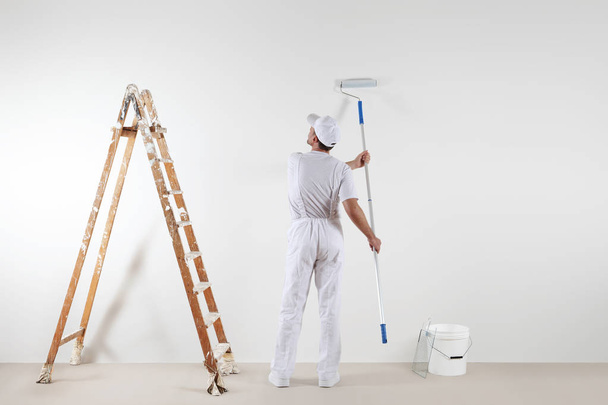 Задний вид художника, смотрящего на чистую стену, с роликовой палкой
 - Фото, изображение
