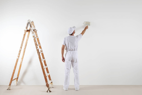 Vista trasera del hombre pintor mirando y pintando la pared en blanco
 - Foto, Imagen