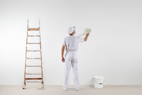 Vista trasera del hombre pintor mirando y pintando la pared en blanco
 - Foto, imagen