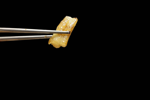 yellow grilled pork fat between silver chopsticks on black backg - Photo, Image