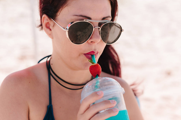 Jovem ruiva bebendo coquetel de morango na praia
 - Foto, Imagem