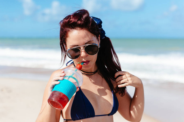 Young redhead woman drinking strawberry cocktail on the beach - Foto, Imagem