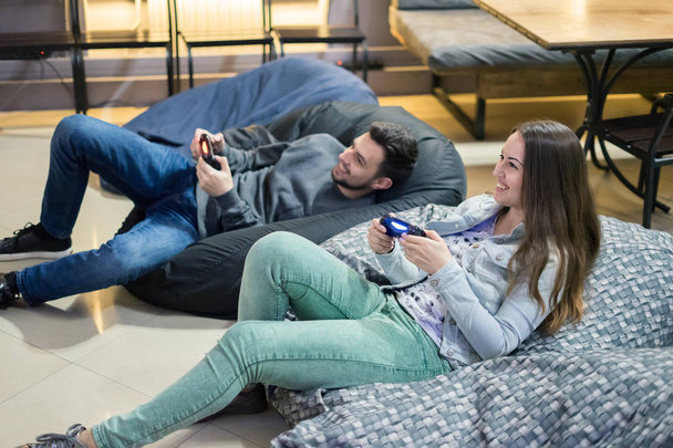 feliz casal amigos jogar jogos de vídeo com joystick sentado na cadeira saco de feijão
 - Foto, Imagem