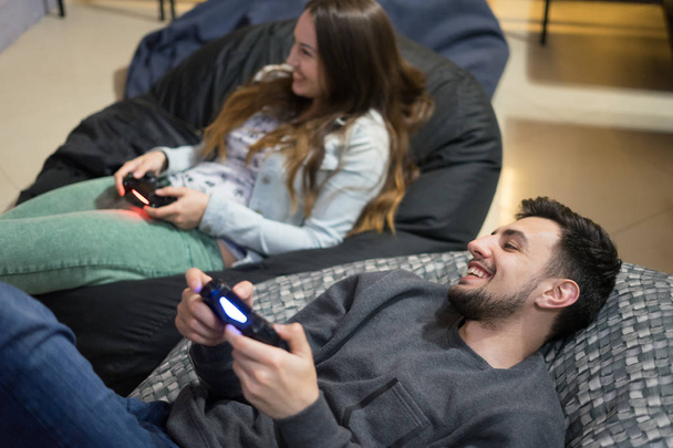 coppia felice amici che giocano ai videogiochi con joystick seduti sulla sedia della borsa del fagiolo
 - Foto, immagini
