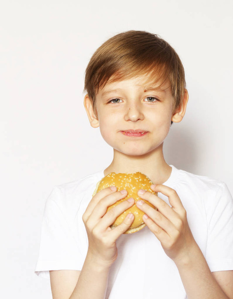Schattige blonde jongen eten cheeseburger - Amerikaanse voedsel - Foto, afbeelding