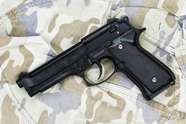 Semi-automatisch pistool op camouflage achtergrond, pistool op militaire textuur, 9 mm pistool, moderne Amerikaanse leger pistool M9. - Foto, afbeelding
