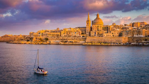 Valletta, Malta - St.Paul's Cathedral in golden hour at Malta's capital city Valletta with sailboat and beautiful colorful sky and clouds - Photo, Image
