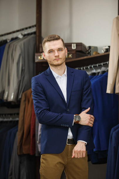 A young stylish man with a beard in a vintage cloth jacket. It is in the showroom, trying on clothes, posing. Advertising photo - Fotografie, Obrázek