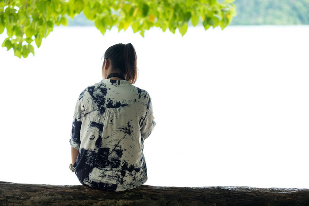 Eine asiatische Frau sitzt auf Holz unter Bäumen und blickt auf die Landschaft. fr - Foto, Bild