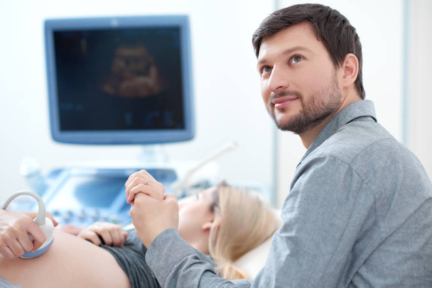 Муж носит беременную жену на ультразвуковом обследовании
. - Фото, изображение