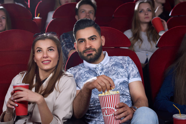 Arabian man and caucasian woman eating popcorn at cinema. - Fotografie, Obrázek