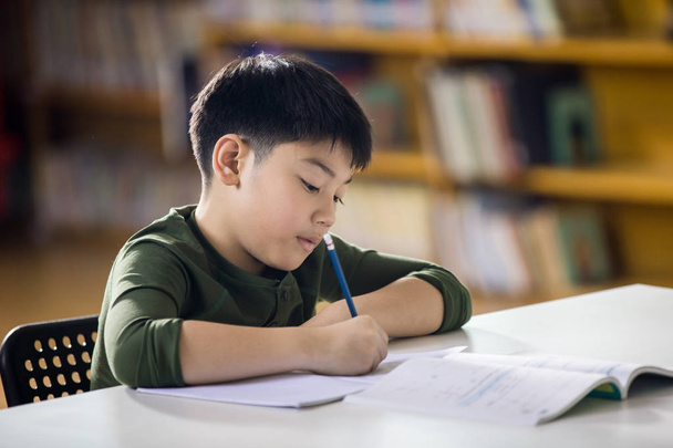 Csinál házi feladatot a mosollyal arcán boldog ázsiai gyermek.  - Fotó, kép