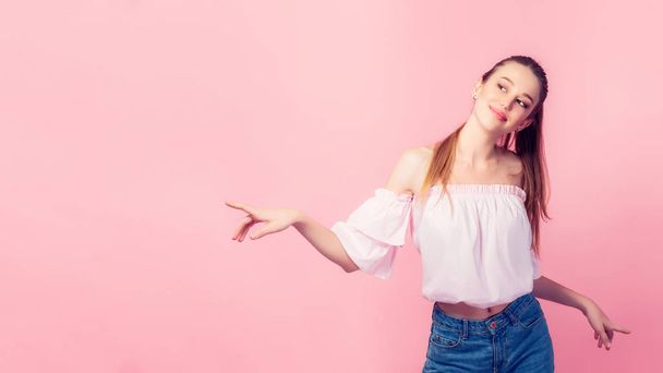 Colorful portrait of happy smiling young woman pointing away against pink wall. - Photo, image