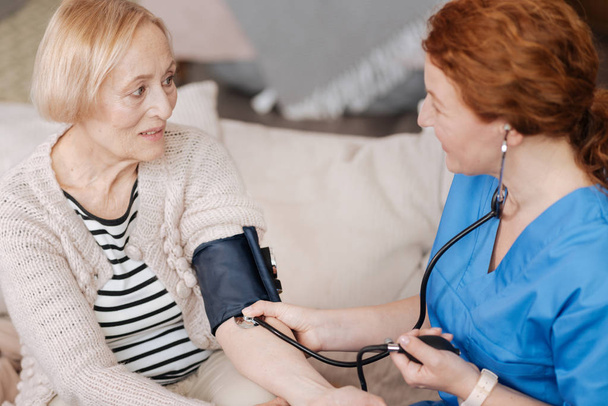 Gentle mindful nurse employing blood pressure sensor - Фото, изображение
