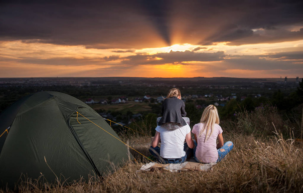 丘の上のキャンプのテントのそばに座って家族 - 写真・画像