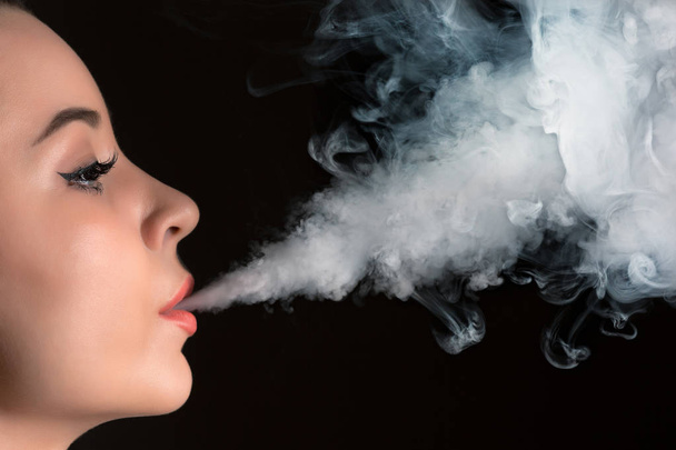 The face of vaping young woman at black studio - Photo, image