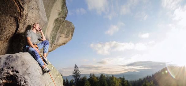 альпинист карабкается по большому валуну на природе с помощью веревки
 - Фото, изображение