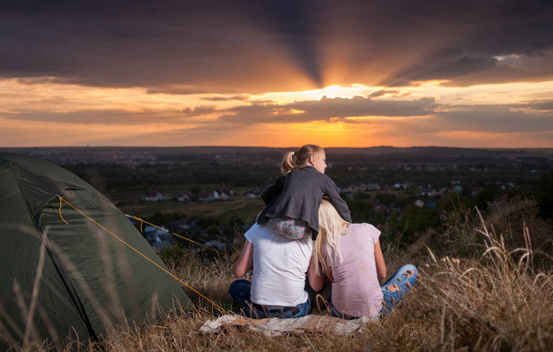 丘の上のキャンプのテントのそばに座って家族 - 写真・画像