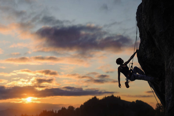 Silhouette of athletic woman climbing steep rock wall - Photo, Image