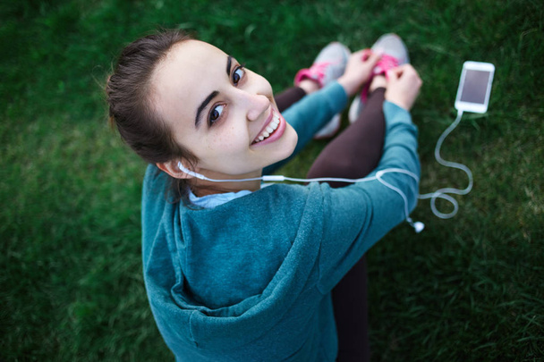 Portrait of young and sporty woman in sportswear Lies with the smartphone on the grass in park - Φωτογραφία, εικόνα