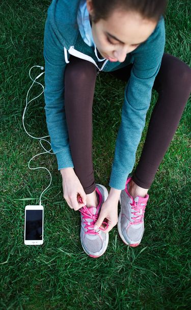 Retrato de mujer joven y deportiva en ropa deportiva Se acuesta con el teléfono inteligente en la hierba en el parque
 - Foto, Imagen