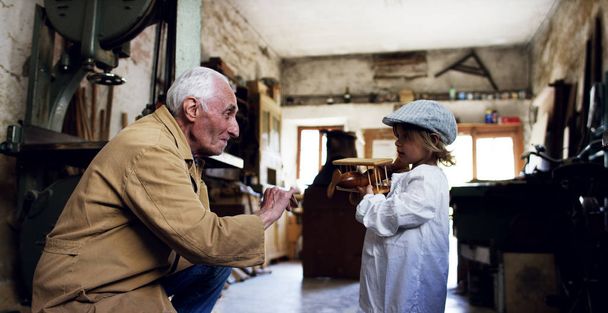 in an old carpentry shop a child and grandfather playing with a wooden airplane concept of tradition that continues over time and surprise - Photo, image
