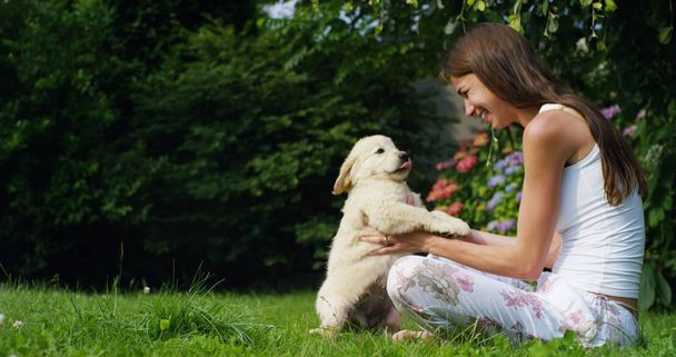 tender mother playing with a sweet puppy golden retriever in a beautiful garden on a sunny day on the grass. friendship concept for dog and vitamins or healthy dog concept. happiness nature animal - Zdjęcie, obraz