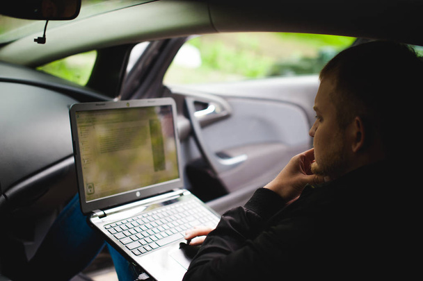 Professional man with a laptop in car tunes tuning control system, updating software - 写真・画像