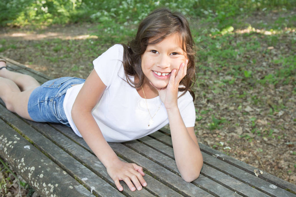 jovem 10 anos de idade menina deitada no jardim banco
 - Foto, Imagem