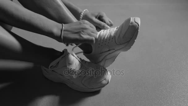 Woman in bodysuit puts on sneakers sitting on floor - Кадри, відео