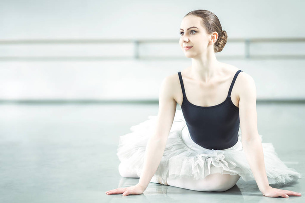 Bellerina sitting on the floor in ballet studio - Фото, изображение