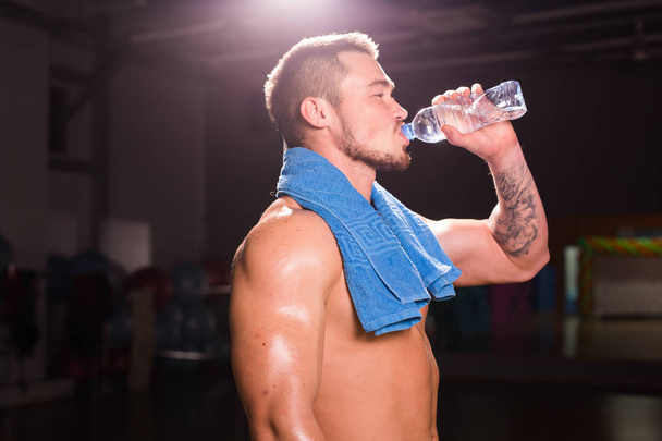 junge kaukasische Bodybuilder in der Turnhalle trinken eine Flasche Wasser. - Foto, Bild