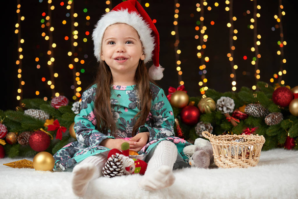 child girl portrait in christmas decoration, happy emotions, winter holiday concept, dark background with illumination and boke lights - Foto, Imagem