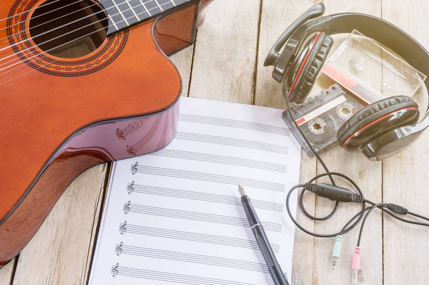 Ακουστική κιθάρα, παρτιτούρες, μεγάλο ακουστικό, πένα, μαγνητοταινίας στον ξύλινο τραπέζι - Φωτογραφία, εικόνα