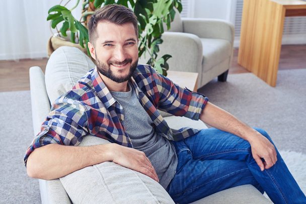 Симпатичный мужчина с голубыми глазами расслабляется на модном диване
 - Фото, изображение
