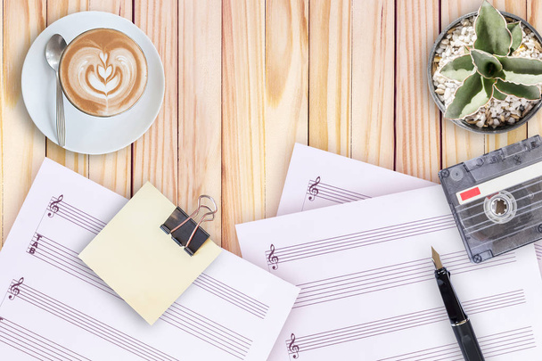 Листовая музыка, кактус, перьевая ручка, кассета и кофе латте на деревянном столе
 - Фото, изображение