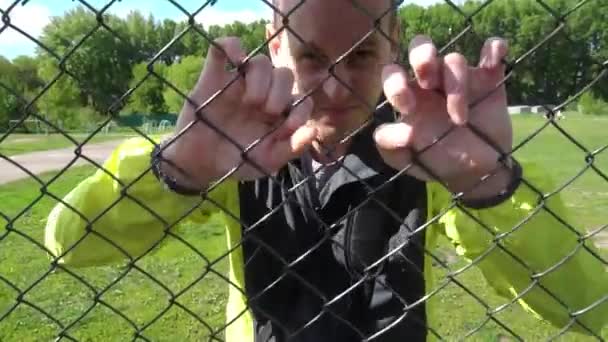 Böser Mann in seinen Zwanzigern, an den Zaun gelehnt, versucht, rauszukommen - Filmmaterial, Video