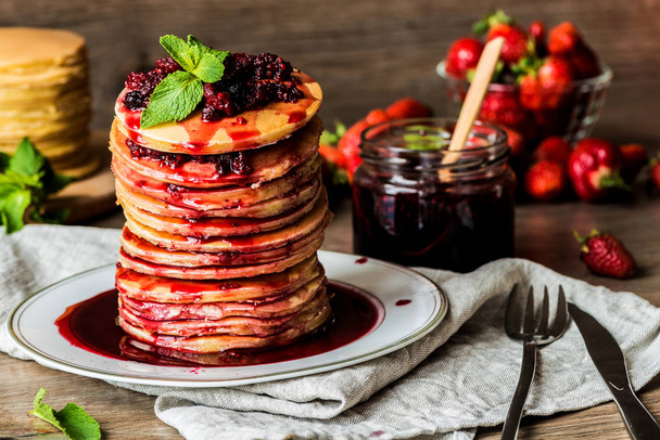 Stapel hausgemachter amerikanischer Pfannkuchen mit Marmelade und Erdbeeren auf hölzernem Hintergrund - Foto, Bild
