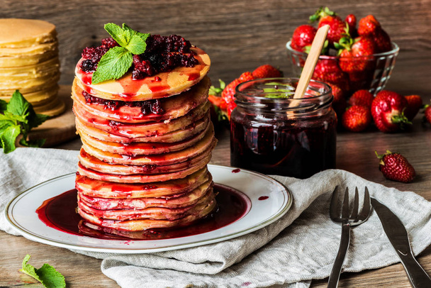 Stapel hausgemachter amerikanischer Pfannkuchen mit Marmelade und Erdbeeren auf hölzernem Hintergrund - Foto, Bild