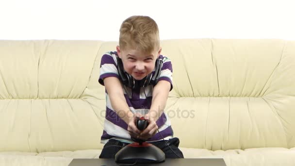 Kid plays with joystick in online game sitting on couch - Video, Çekim