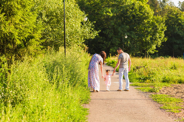 Семья, паркур и люди - счастливые мама, папа и маленькая девочка, гуляющие в летнем парке
 - Фото, изображение