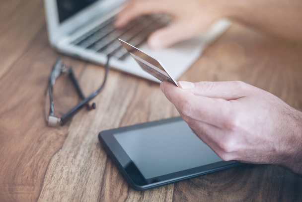 homme assis au bureau en bois rustique tenant une carte de crédit tout en tapant sur un ordinateur portable
 - Photo, image