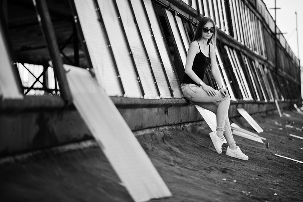 Girl at sunglasses and jeans posed at the roof of abadoned indus - 写真・画像