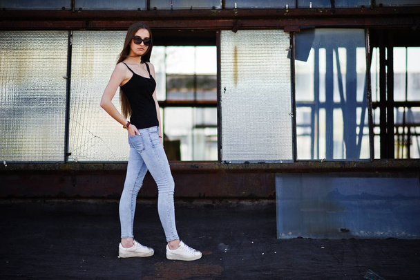 Girl at sunglasses and jeans posed at the roof of abadoned indus - 写真・画像