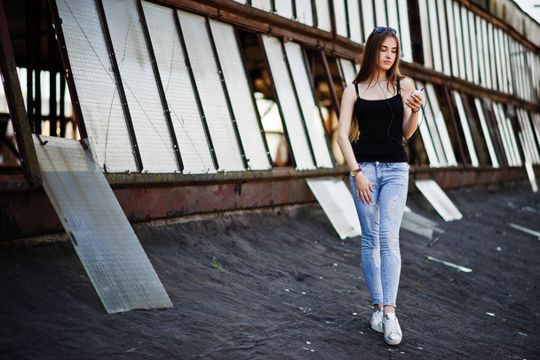 Girl at sunglasses and jeans, with phone and headphones posed at - Fotó, kép
