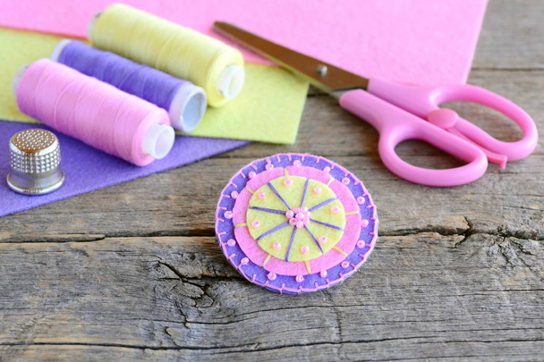 Felt round flower decorated with beads. Handmade cute round felt flower, scissors, thread, colored felt sheets, thimble on vintage wooden background. Simple and quick kids sewing project  - Photo, Image