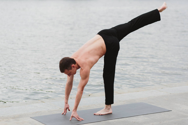 a young man practicing yoga asanas in the city on the waterfront - Фото, зображення