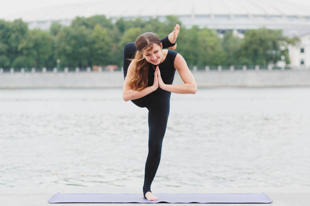 a young woman practicing yoga asanas in the city on the waterfro - Foto, Imagem
