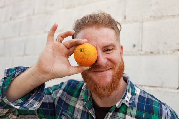 bärtiger Mann bedeckt Auge mit Orange - Foto, Bild