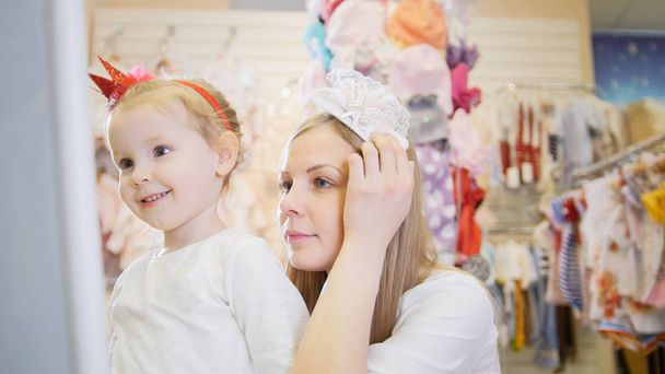 Children shopping - mom tries on a white headband next to his daughter - Photo, Image